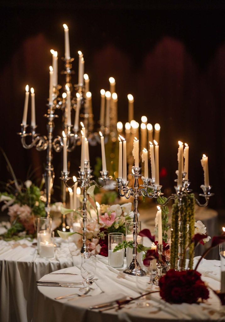 Elegant wedding reception table with silver candelabras, white taper candles, and lush floral arrangements of blush pink and deep red roses.